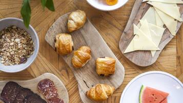 A wooden table with various food items including croissants, cheese, and watermelon slices.