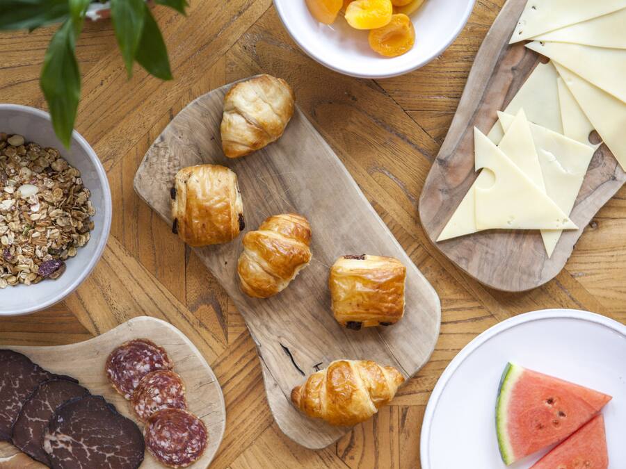 A wooden table with various food items including croissants, cheese, and watermelon slices.
