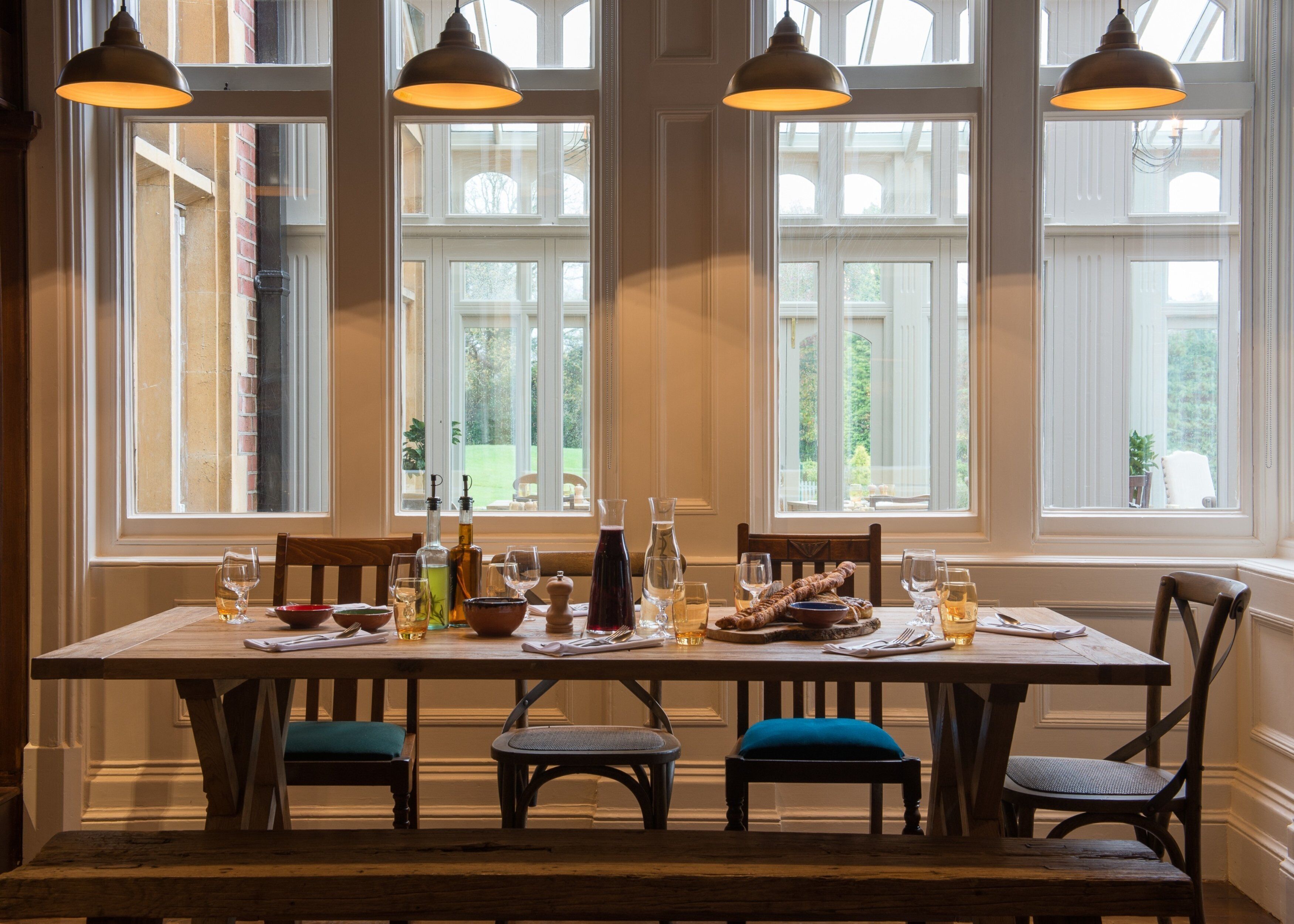 A dining table set for four with a view of a garden through large windows.