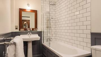 Un baño con un lavamanos blanco, una bañera, una ducha con mampara de vidrio y un espejo con marco de madera.