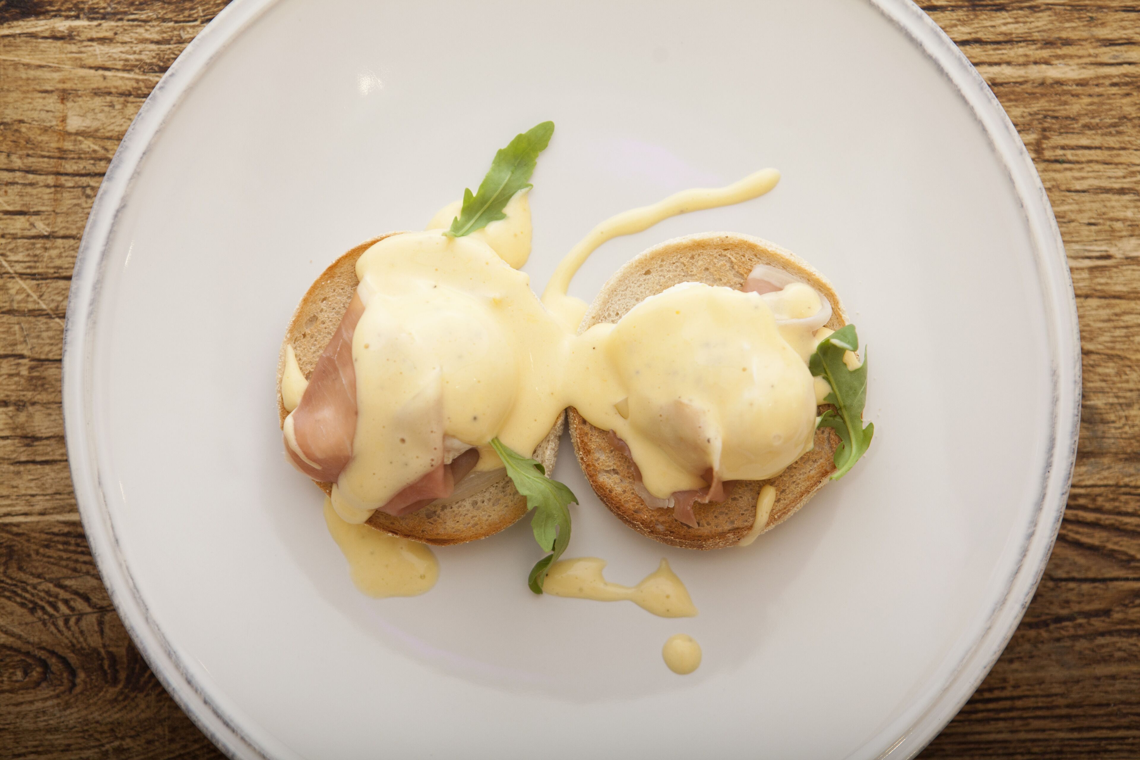 Une assiette avec deux tranches de pain grillé garnies de jambon et d’œuf, décorée d’une feuille et nappée de sauce.