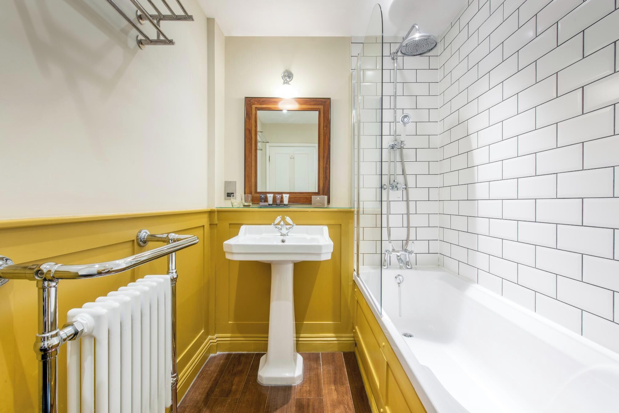 A bathroom with a white bathtub, a pedestal sink, and a mirror above it.
