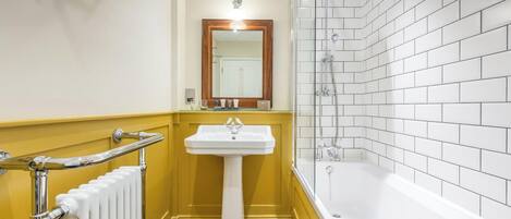 A bathroom with a white bathtub, a pedestal sink, and a mirror above it.