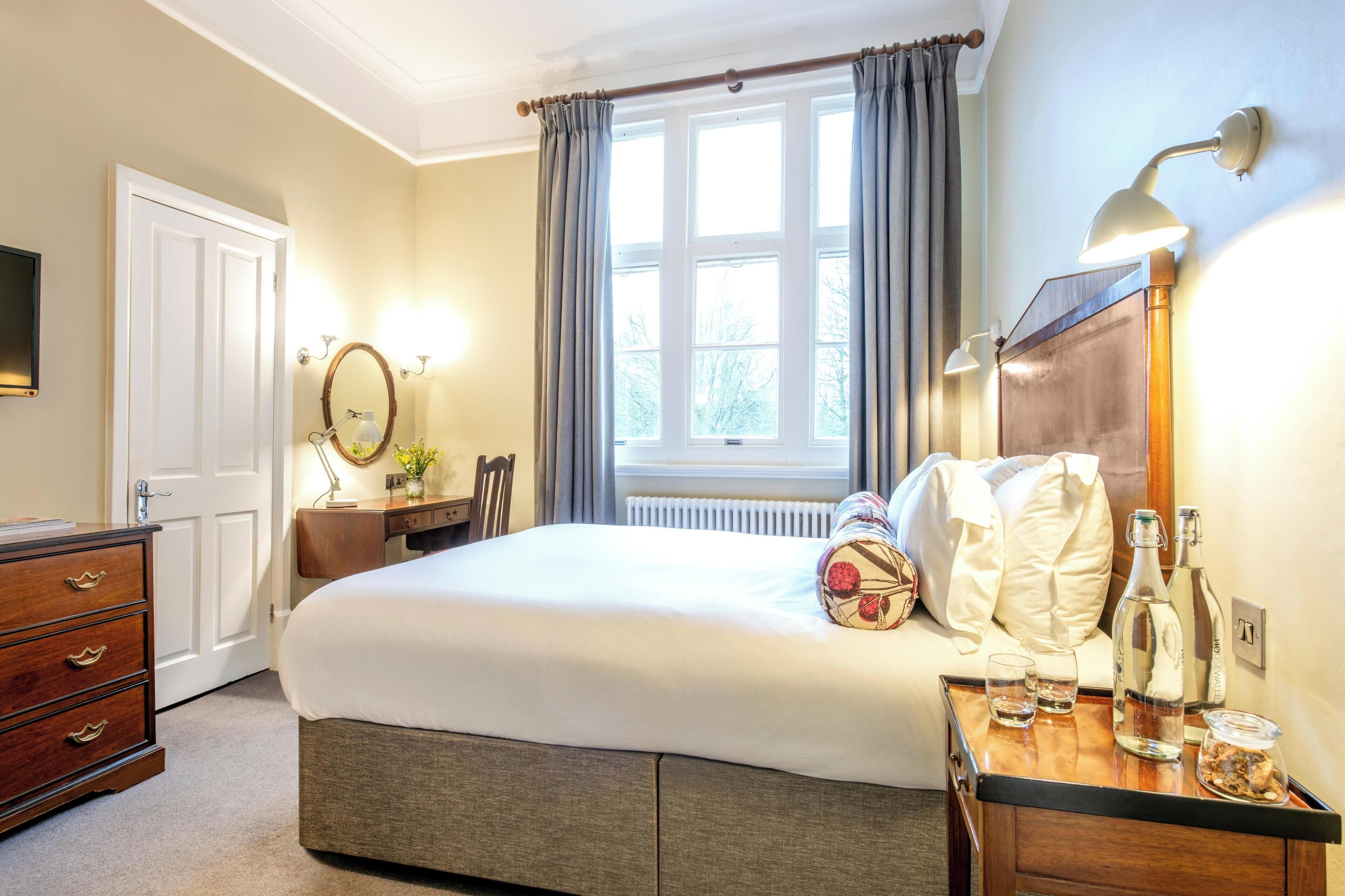 Une chambre d’hôtel équipée d’un lit, d’une table de chevet, d’une lampe et offrant une vue sur l’extérieur par une fenêtre.