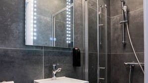 Un bany modern amb dutxa de vidre, un lavabo blanc i un mirall amb il·luminació.