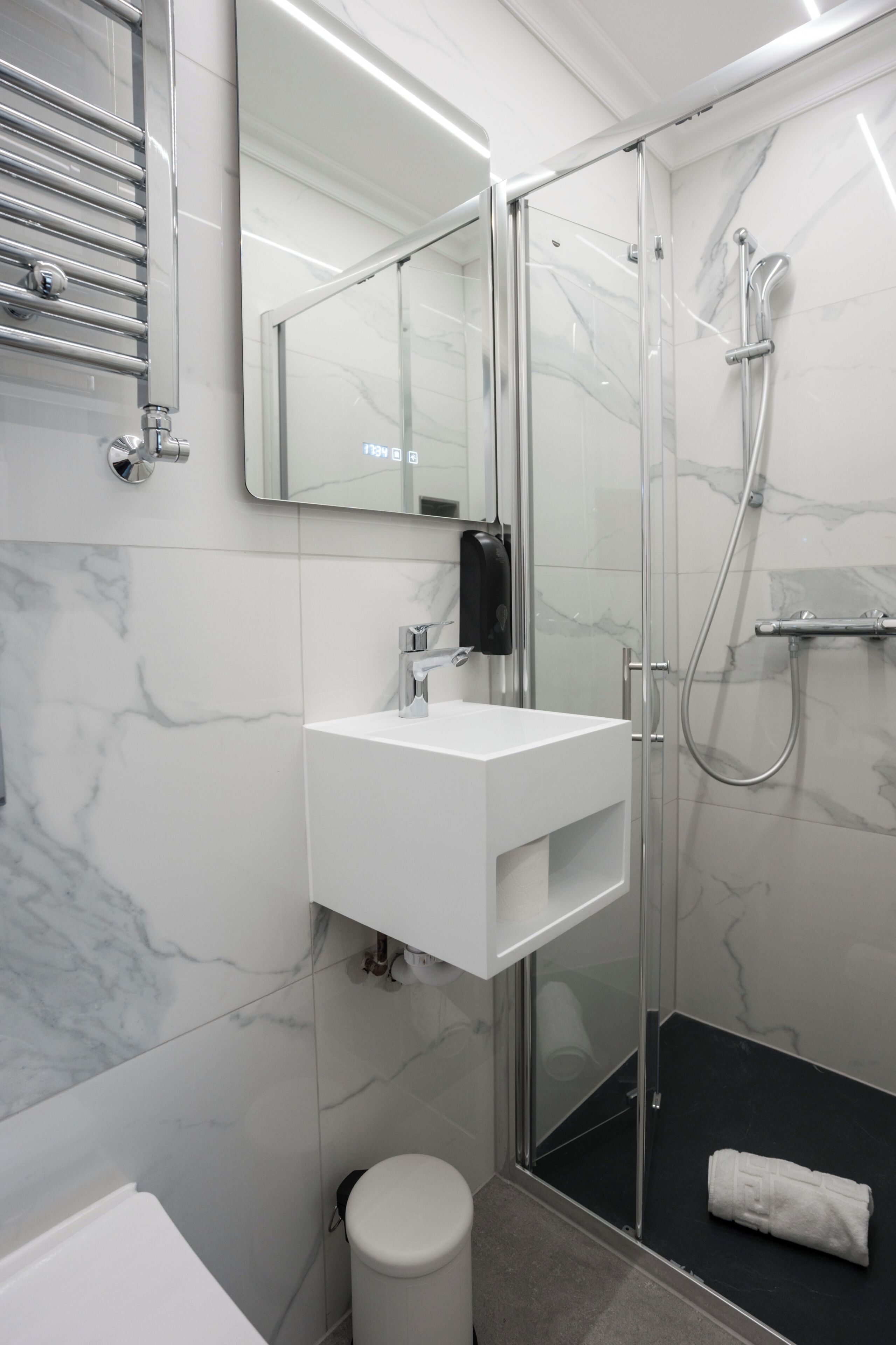 Un baño moderno con cabina de ducha de vidrio, un lavamanos blanco y pared con azulejos de mármol.