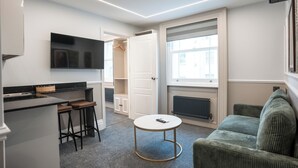 Un apartament modern amb cuina, zona de menjador, sala d'estar amb sofà i televisió penjada a la paret.