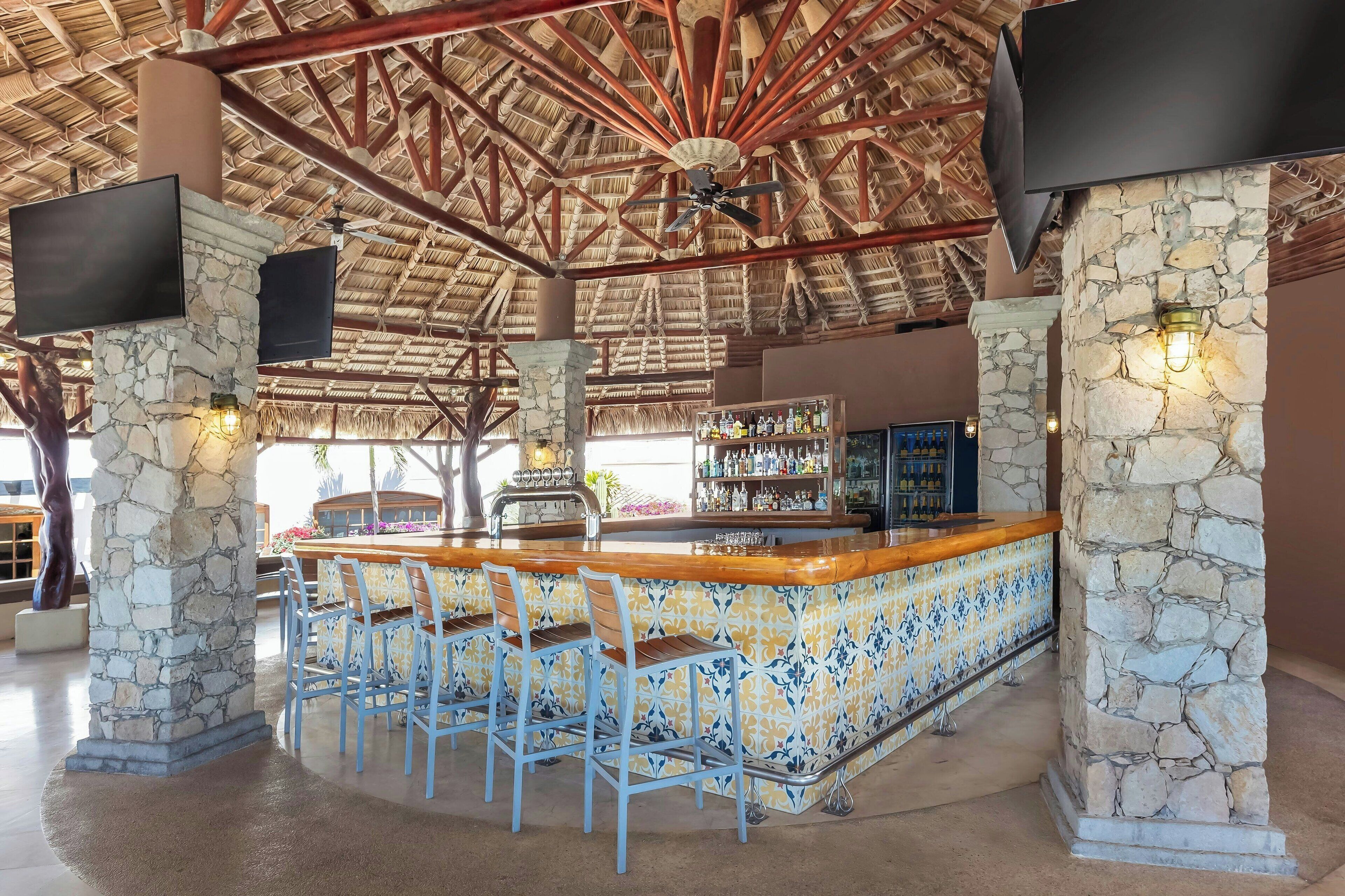 Angolo bar con pilastri in pietra, sgabelli blu e rivestimento a mosaico.