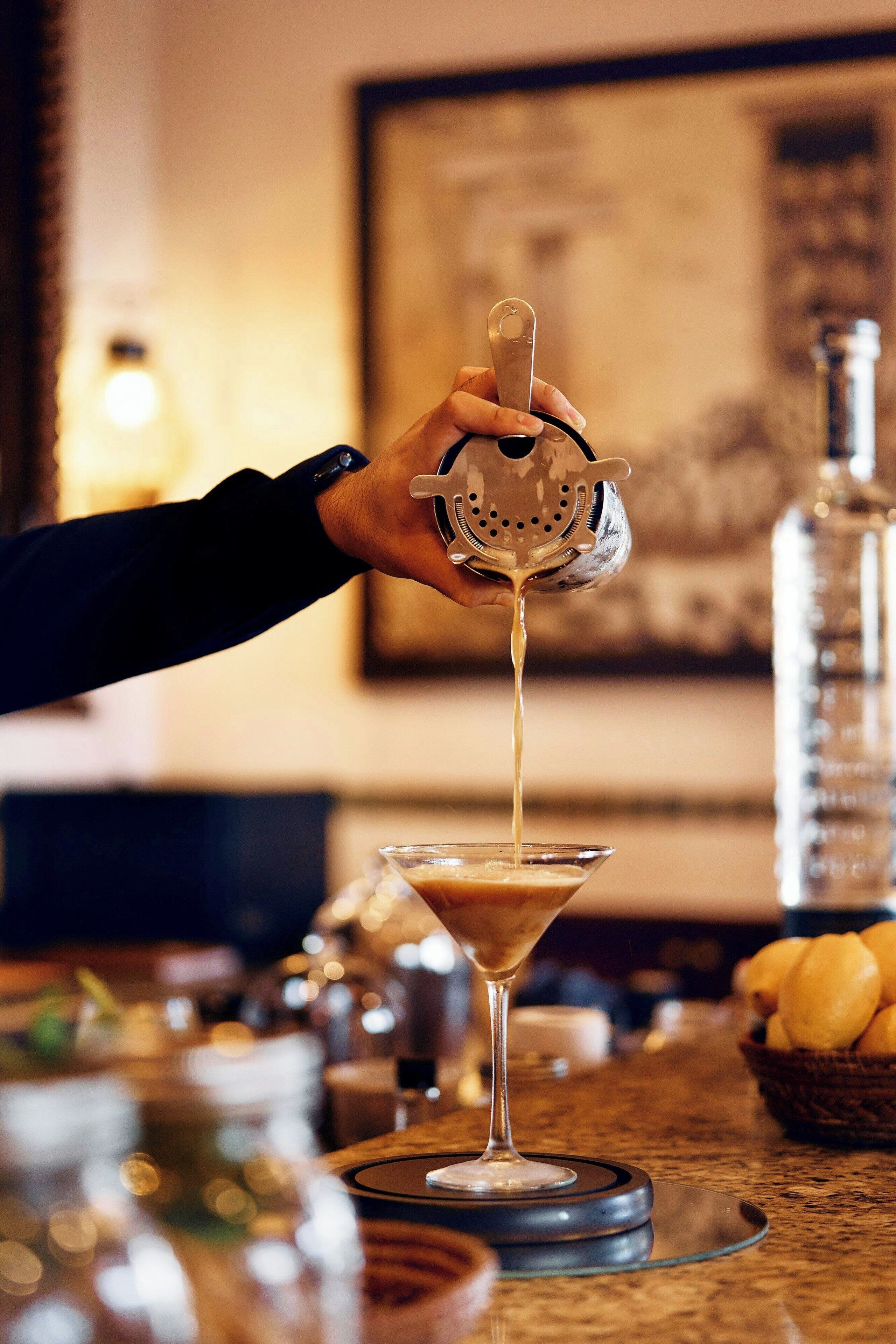 A hand pouring a drink into a martini glass.