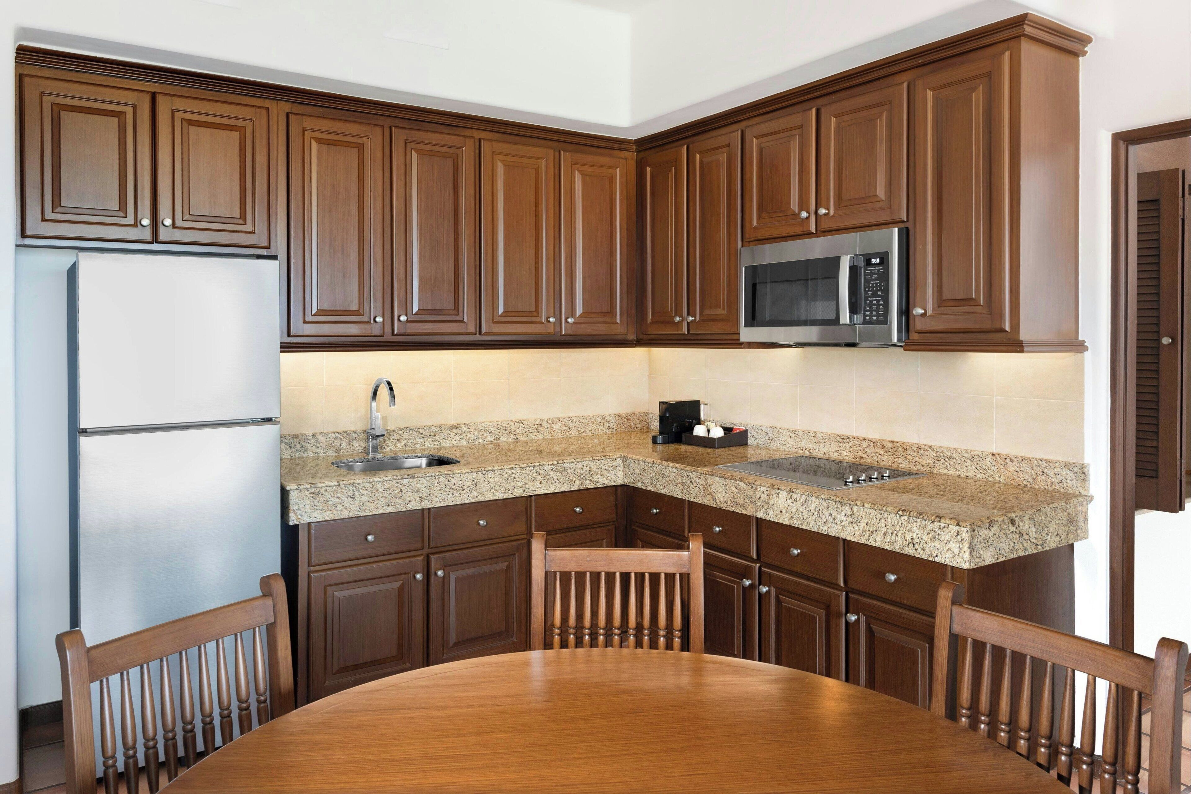 A kitchen with wooden cabinets, a stainless steel refrigerator, a microwave, and a granite countertop.