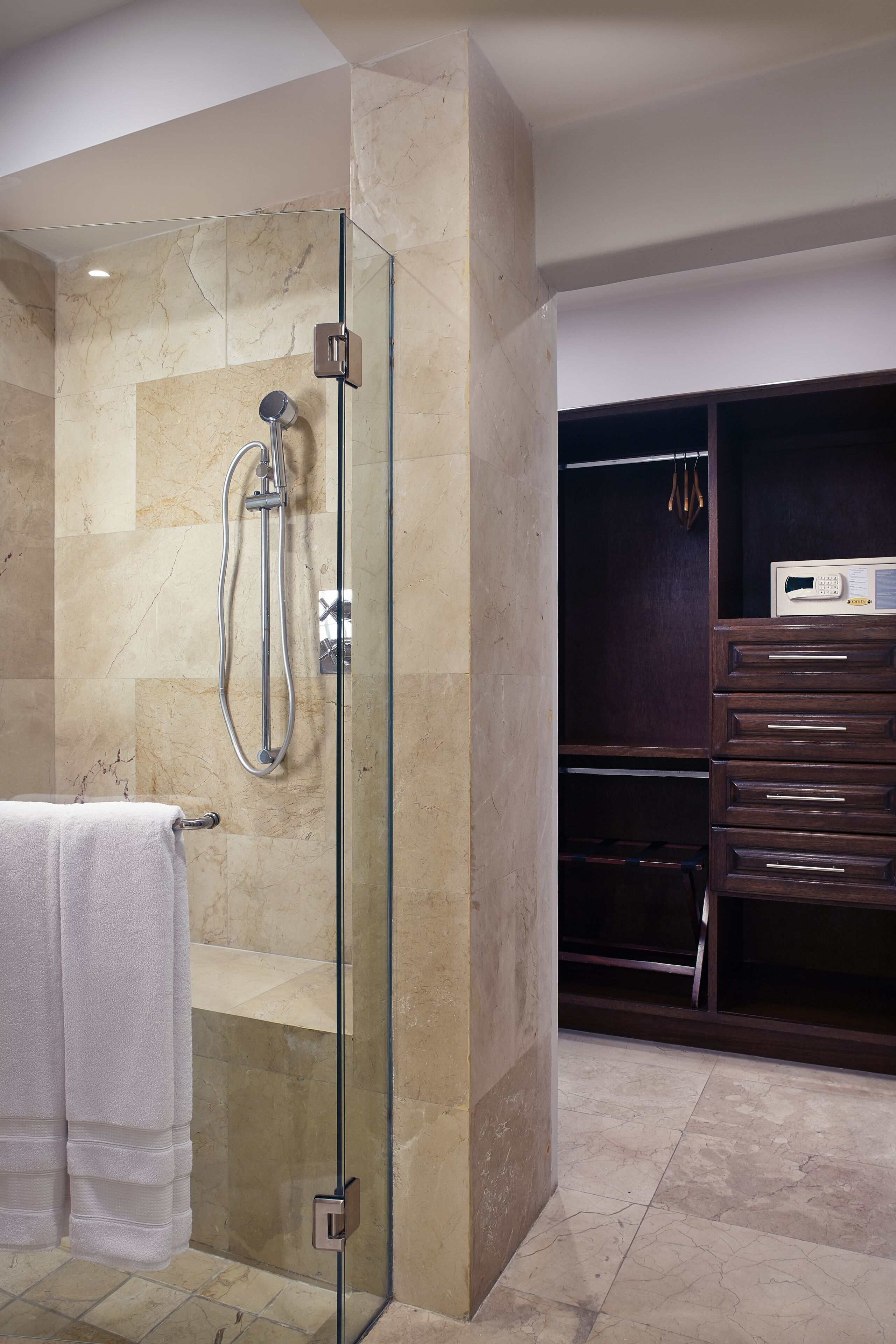 Ein modernes Badezimmer mit einer gläsernen Duschkabine, Marmorfliesen, einem weißen Handtuch und einem dunklen Holzwaschtisch mit Schubladen.