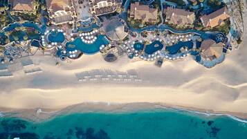 Vista aérea de un resort con múltiples piscinas, villas frente a la playa y una playa de arena.