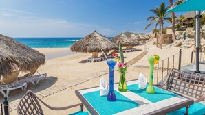 Eine Strandbar mit Reetdachschirmen, Liegestühlen und einem Tisch mit Getränken und einer Speisekarte.