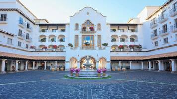 A courtyard with a fountain, white buildings with balconies, and a tiled floor.