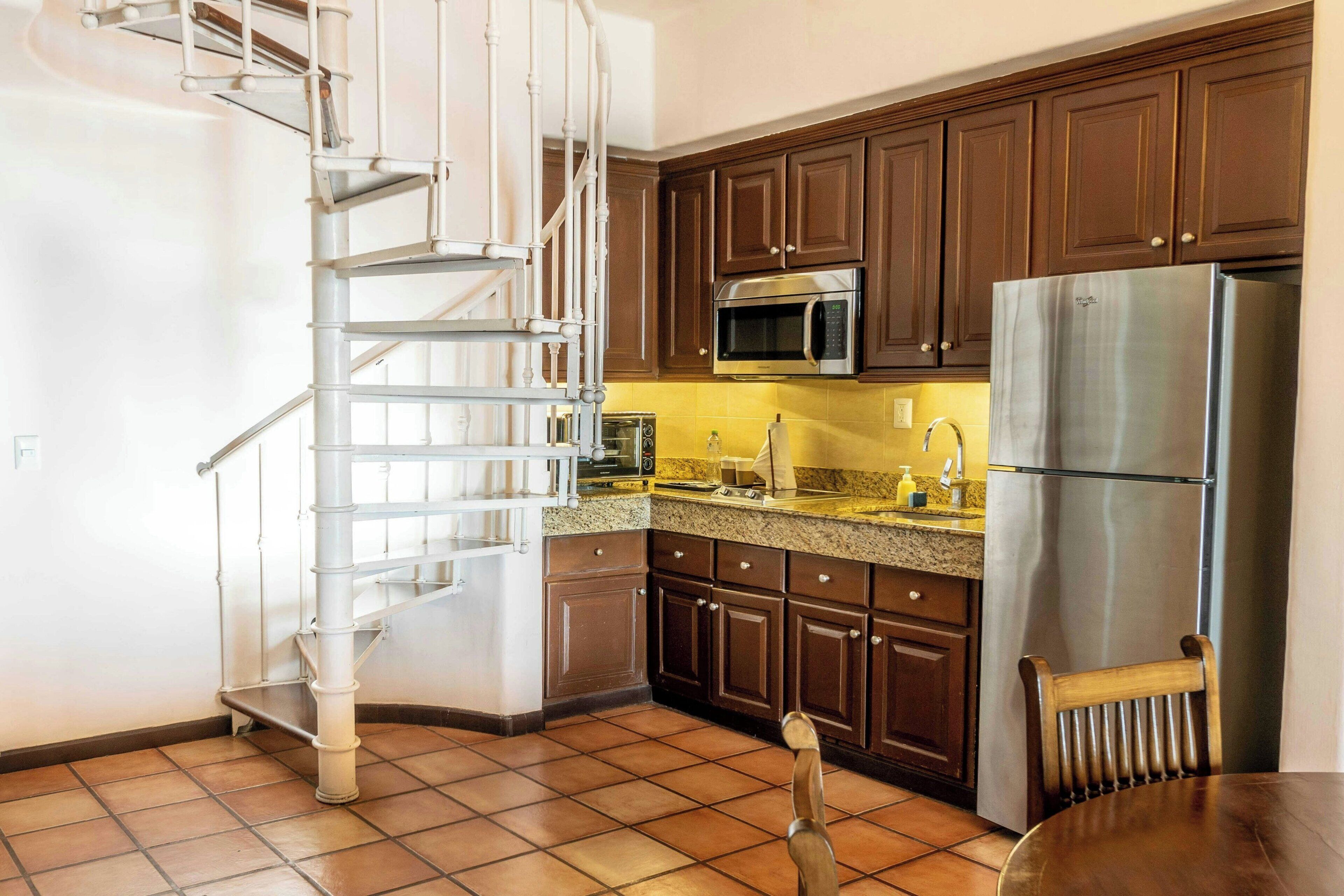 Una cocina con armarios de madera oscura, electrodomésticos de acero inoxidable y una escalera espiral blanca.