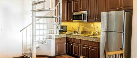 Una cocina con armarios de madera oscura, electrodomésticos de acero inoxidable y una escalera espiral blanca.