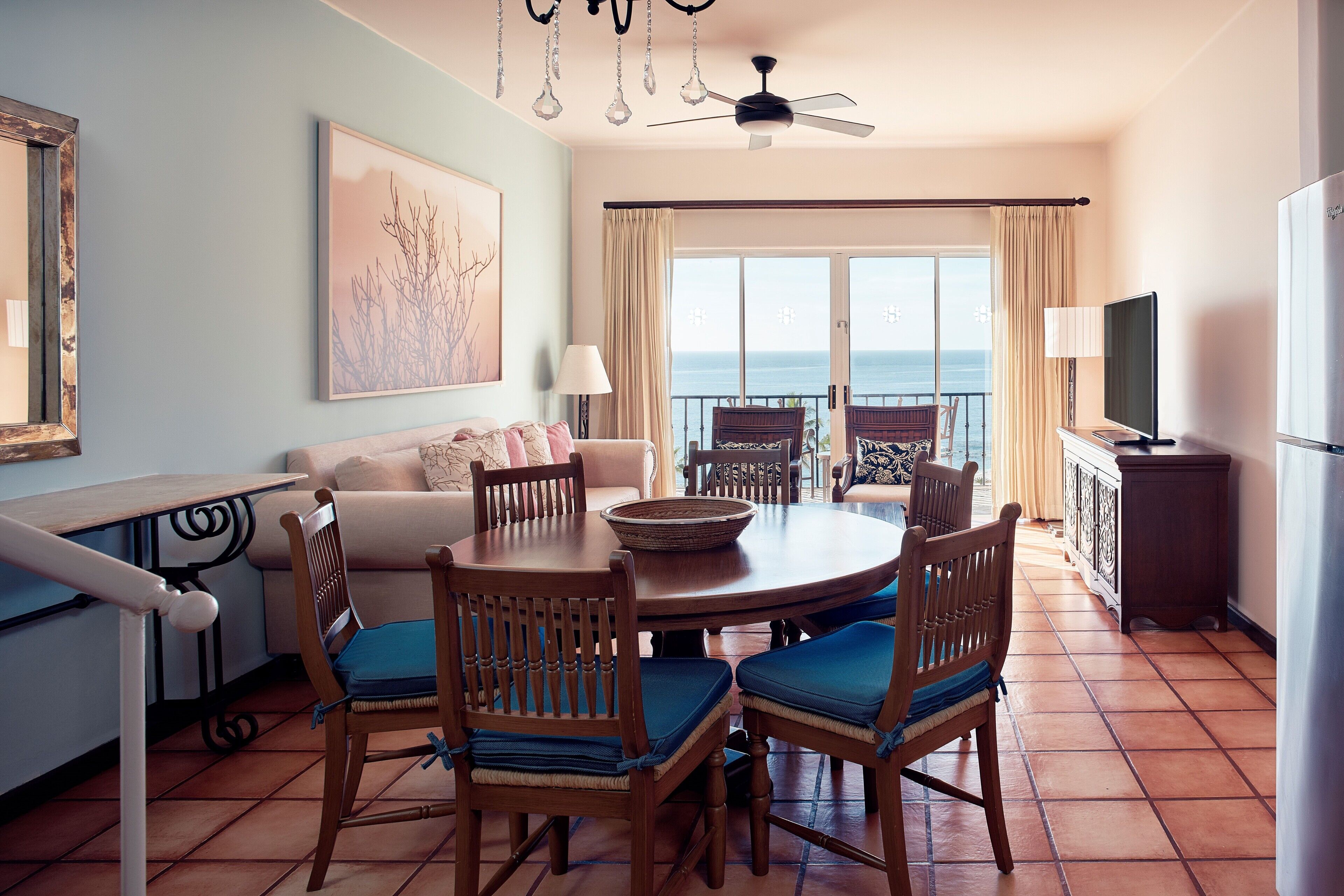 A dining area with a round table, chairs, and a view of the ocean through large windows.