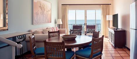 A dining area with a round table, chairs, and a view of the ocean through large windows.