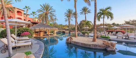 A resort pool area with lounge chairs, palm trees, and a thatched-roof structure.