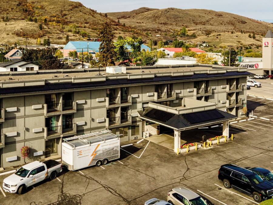 Un hotel de varios pisos con estacionamiento, un letrero de Quality Inn & Suites by Choice Hotels, y montañas al fondo.