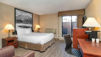 Quarto de hotel com uma cama grande, duas luminárias de cabeceira, uma escrivaninha com cadeira, uma televisão e um quadro na parede.