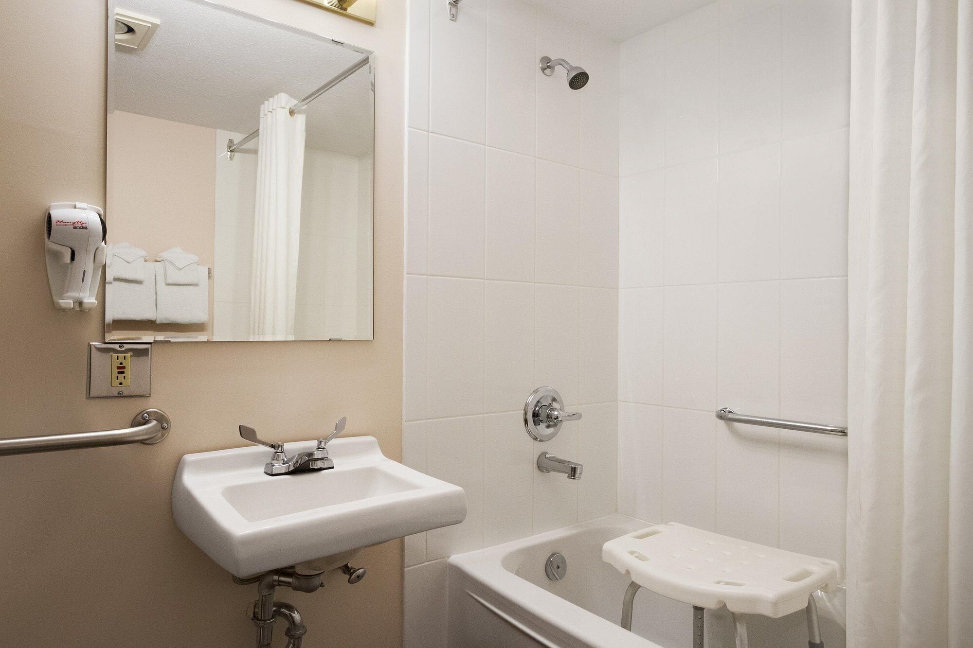 A bathroom with a sink, mirror, shower, and a small stool.