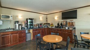 A compact kitchen with a microwave, coffee maker, and refrigerator. There are wooden cabinets and a dining area with chairs. - Quality Inn & Suites (Vernon)