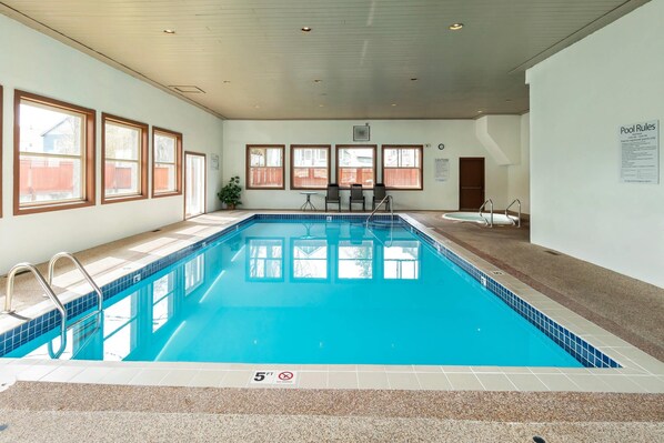 An indoor swimming pool with clear pool rules, a 5 ft depth marker, and a view of the outside through large windows.