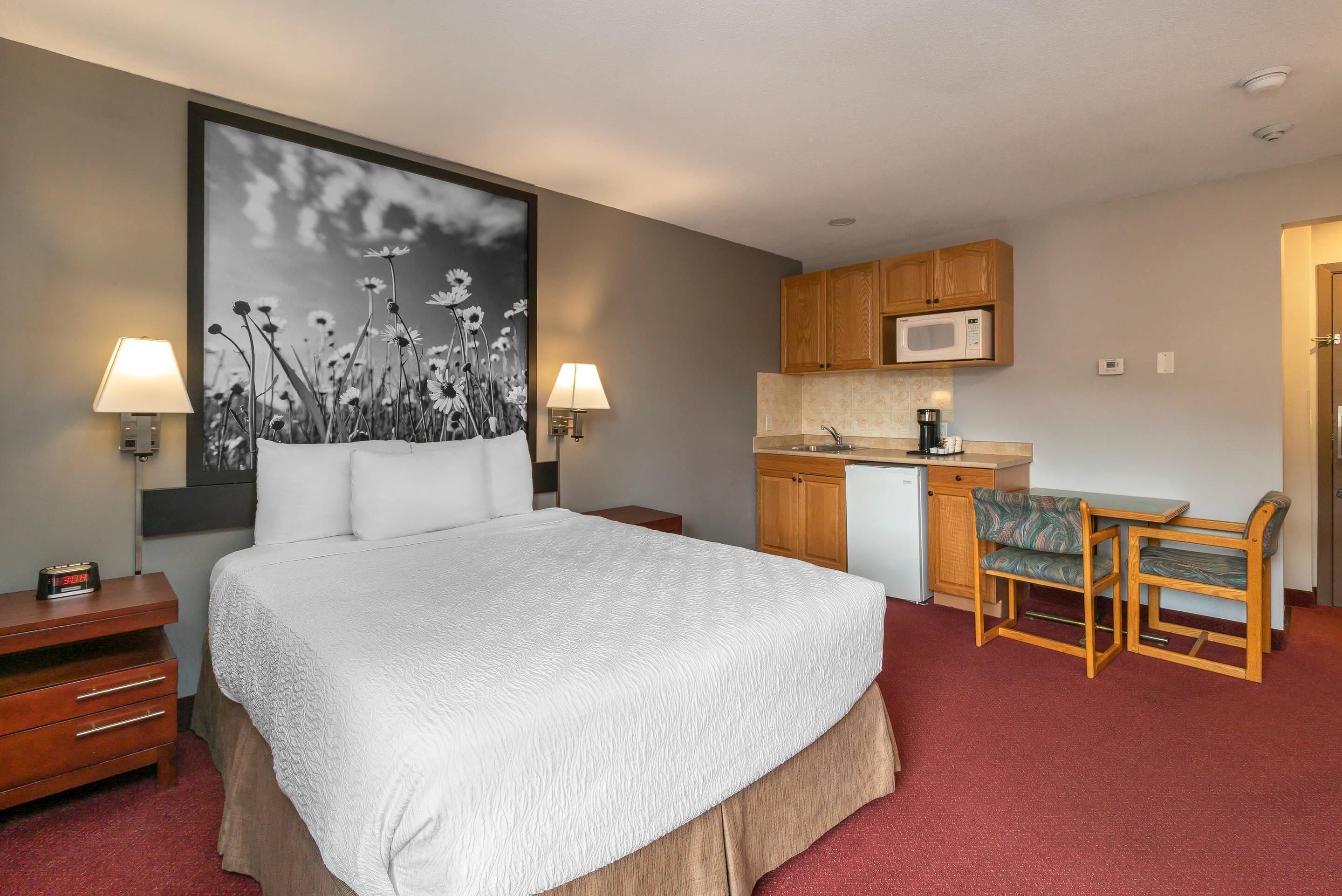 Habitación de hotel con cama, lámparas de noche, escritorio con silla, microondas y kitchenette.