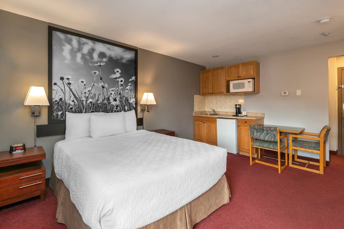 A hotel room with a bed, bedside lamps, a desk with a chair, a microwave, and a kitchenette.