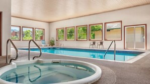 Een binnenzwembad met een jacuzzi, omringd door ramen met uitzicht op groen en gebouwen.
