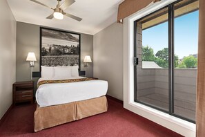 A hotel room with a bed, two bedside lamps, a ceiling fan, a large window, and a framed picture on the wall.