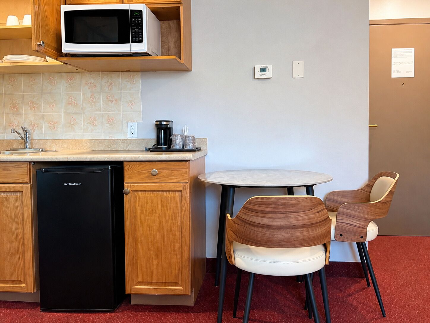 A compact kitchen with a microwave, coffee maker, and dishwasher. There is a small round table with two chairs.