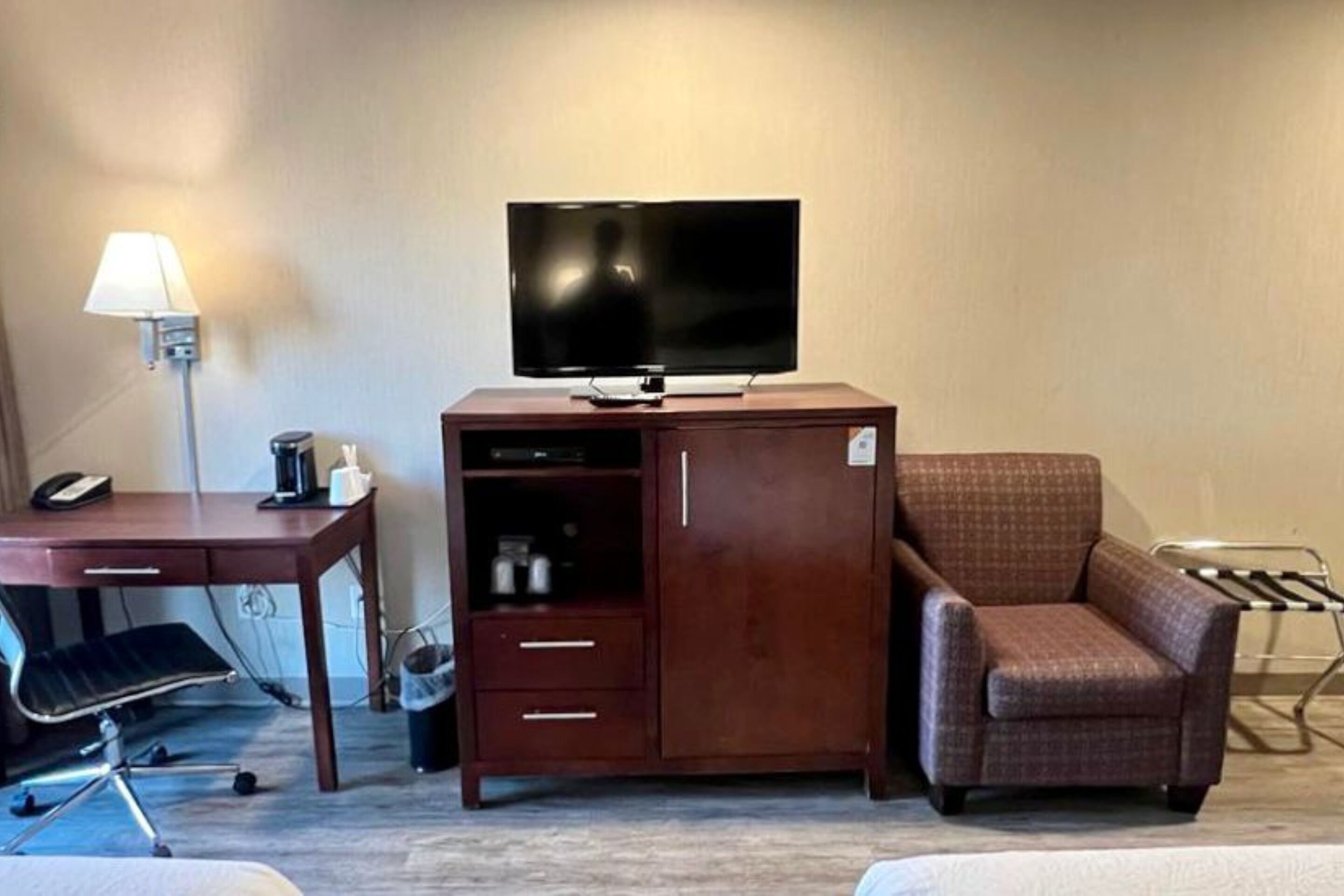 A hotel room with a wooden desk, a television on a cabinet, a chair, and a bed.
