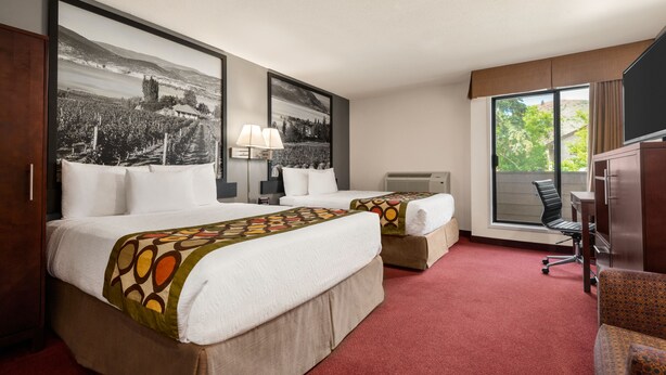 Een hotelkamer met twee bedden, een bureau, een stoel, een televisie en grote ramen.