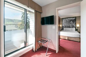 Una habitación de hotel con cama, televisión, ventana con cortinas y vista al exterior.