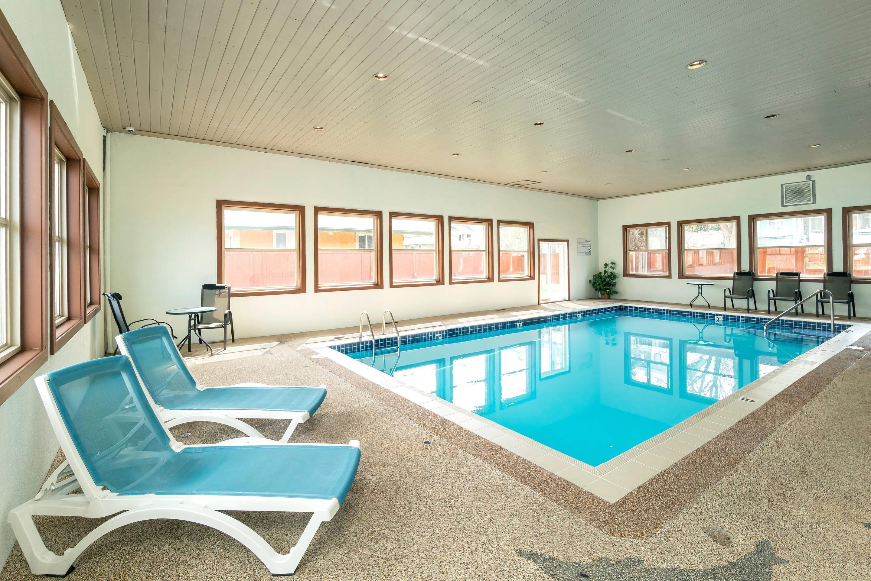 An indoor swimming pool with blue water, surrounded by lounge chairs and a small table.