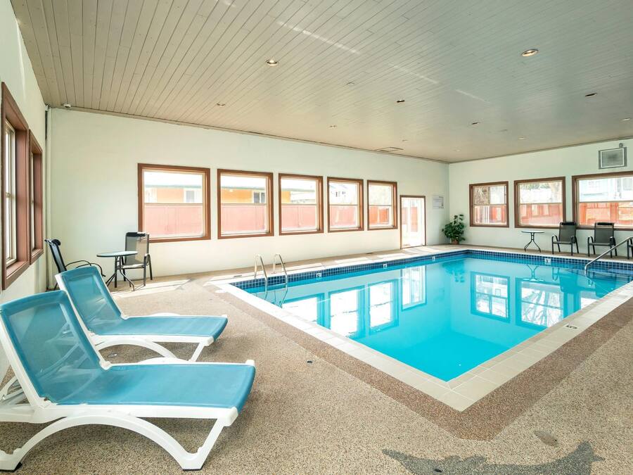 Una piscina interior con agua azul, rodeada de sillas de descanso y una mesita.