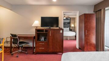 A hotel room with a bed, a desk with a television, a chair, a wardrobe, and a bathroom visible through an open door.