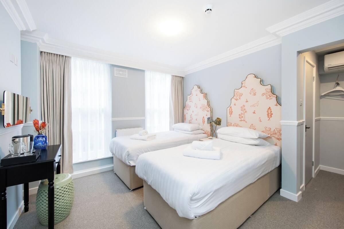 A hotel room with two beds, a desk, a mirror, and a wardrobe.