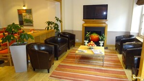 A living room with leather sofas, a flat-screen TV, a fireplace, and potted plants. - Americana Hotel (London)