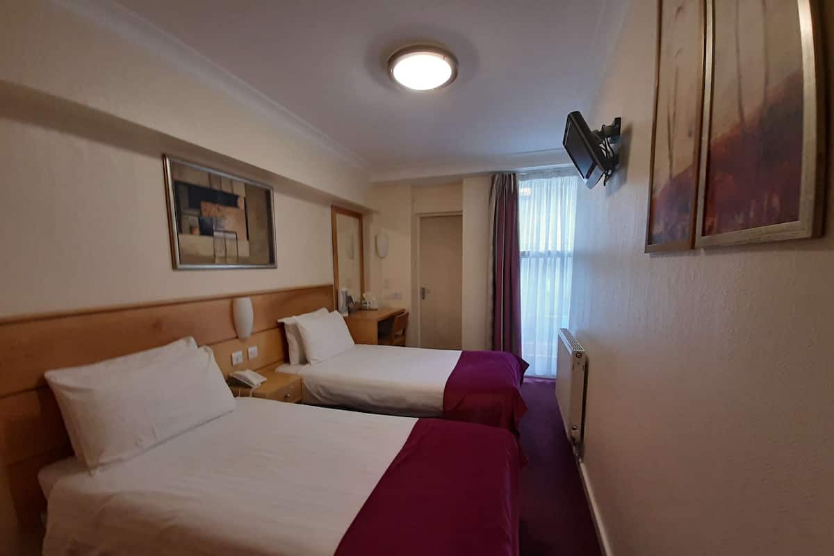 A hotel room with two beds, a desk, a telephone, a mirror, and a television mounted on the wall.