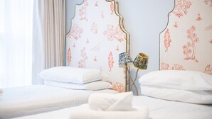 A hotel room with two beds, each with white bedding and decorative headboards featuring floral patterns. - Americana Hotel (London)