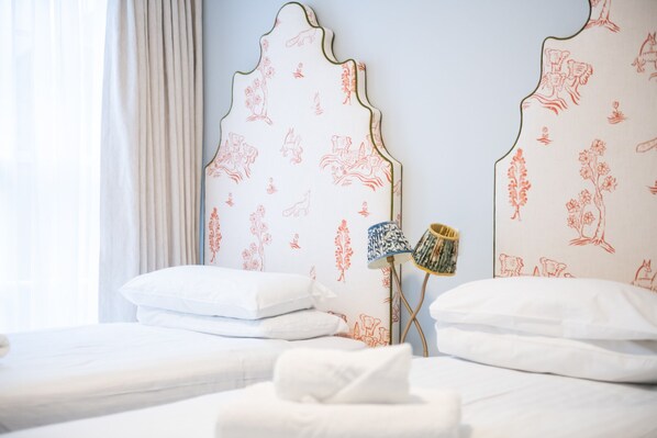 A hotel room with two beds, each with white bedding and decorative headboards featuring floral patterns. - Americana Hotel (London)