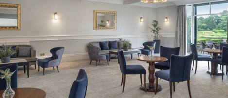 A spacious hotel lobby with a high ceiling, elegant chandeliers, comfortable seating, and large windows offering a view of the outdoors.