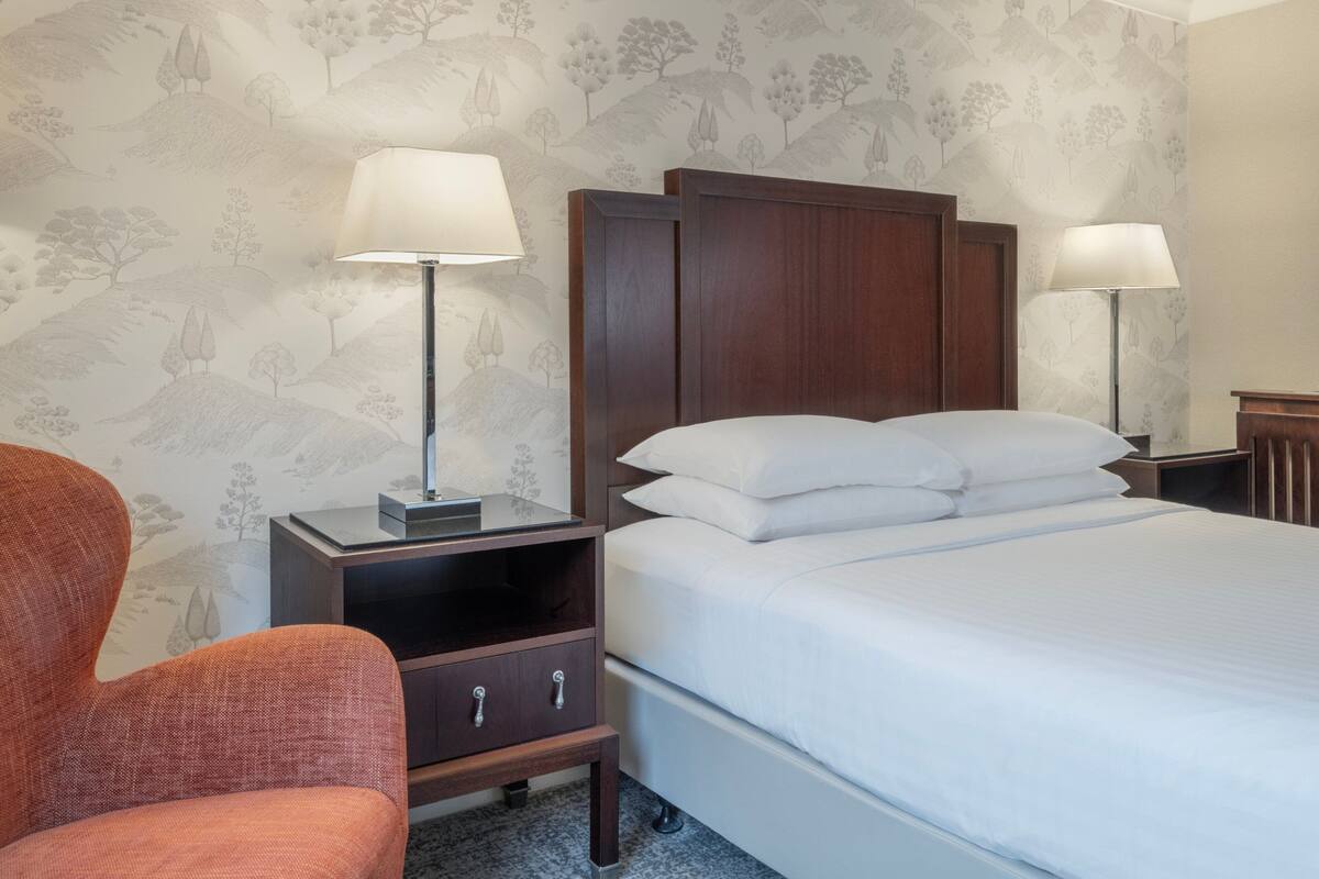 A neatly arranged hotel room with a bed, two bedside tables with lamps, a nightstand, and a chair.
