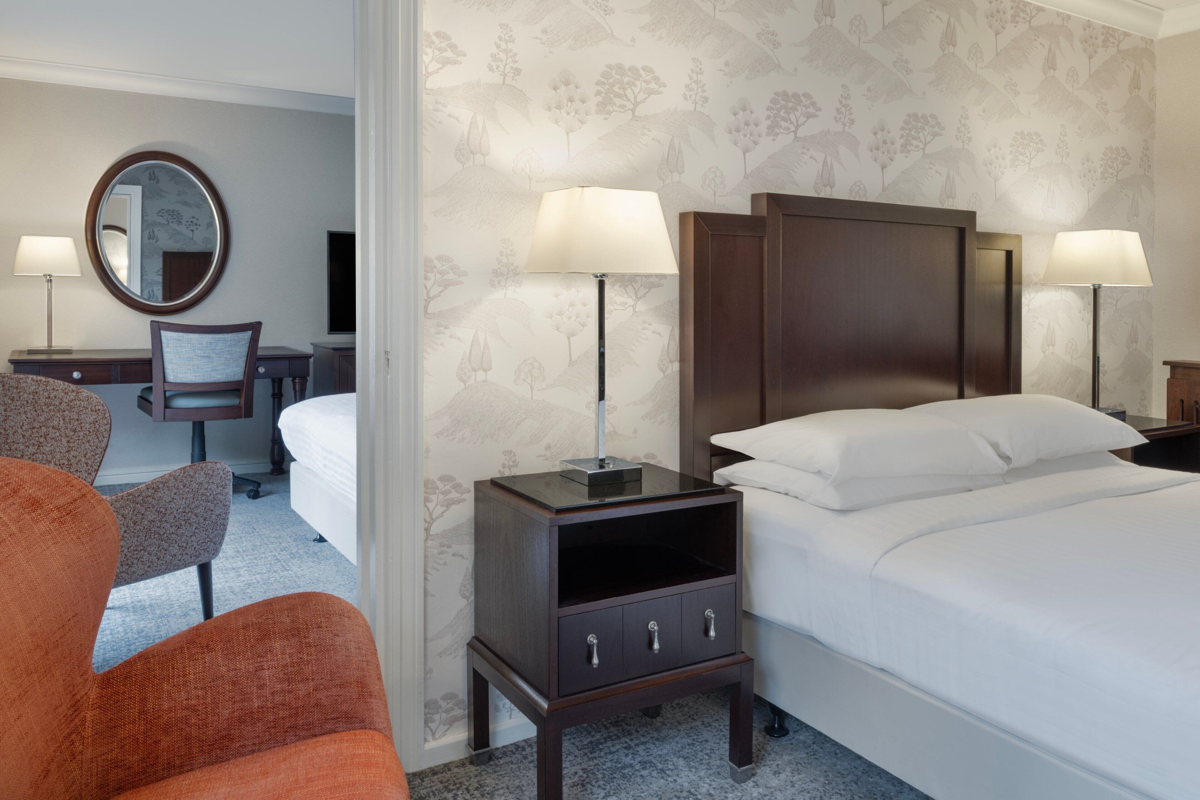 A hotel room with a bed, two bedside tables with lamps, a chair, a desk, and a mirror.