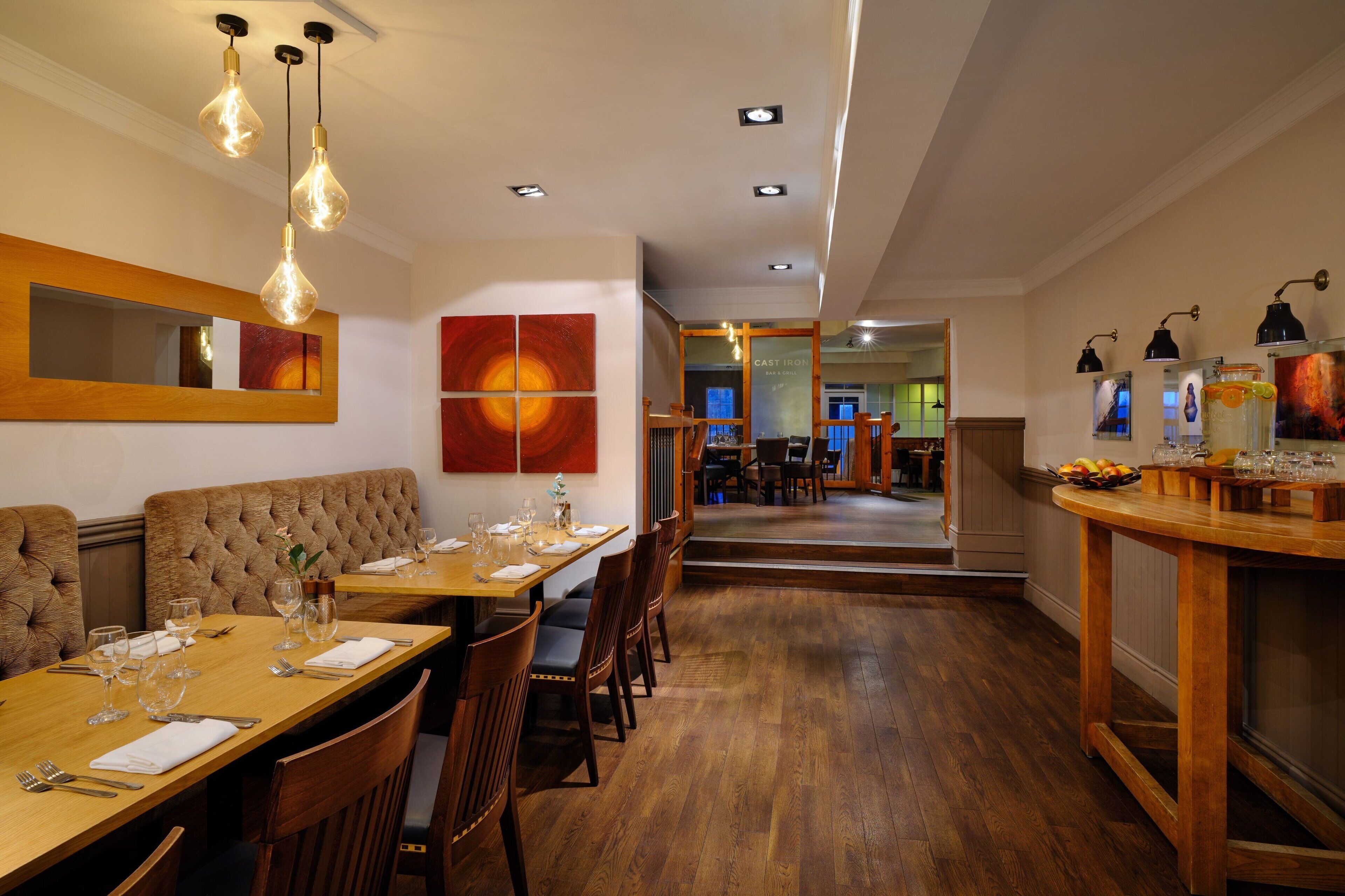 A restaurant with wooden tables and chairs, hanging light fixtures, and artwork on the walls.