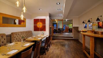 A restaurant with wooden tables and chairs, hanging light fixtures, and artwork on the walls.