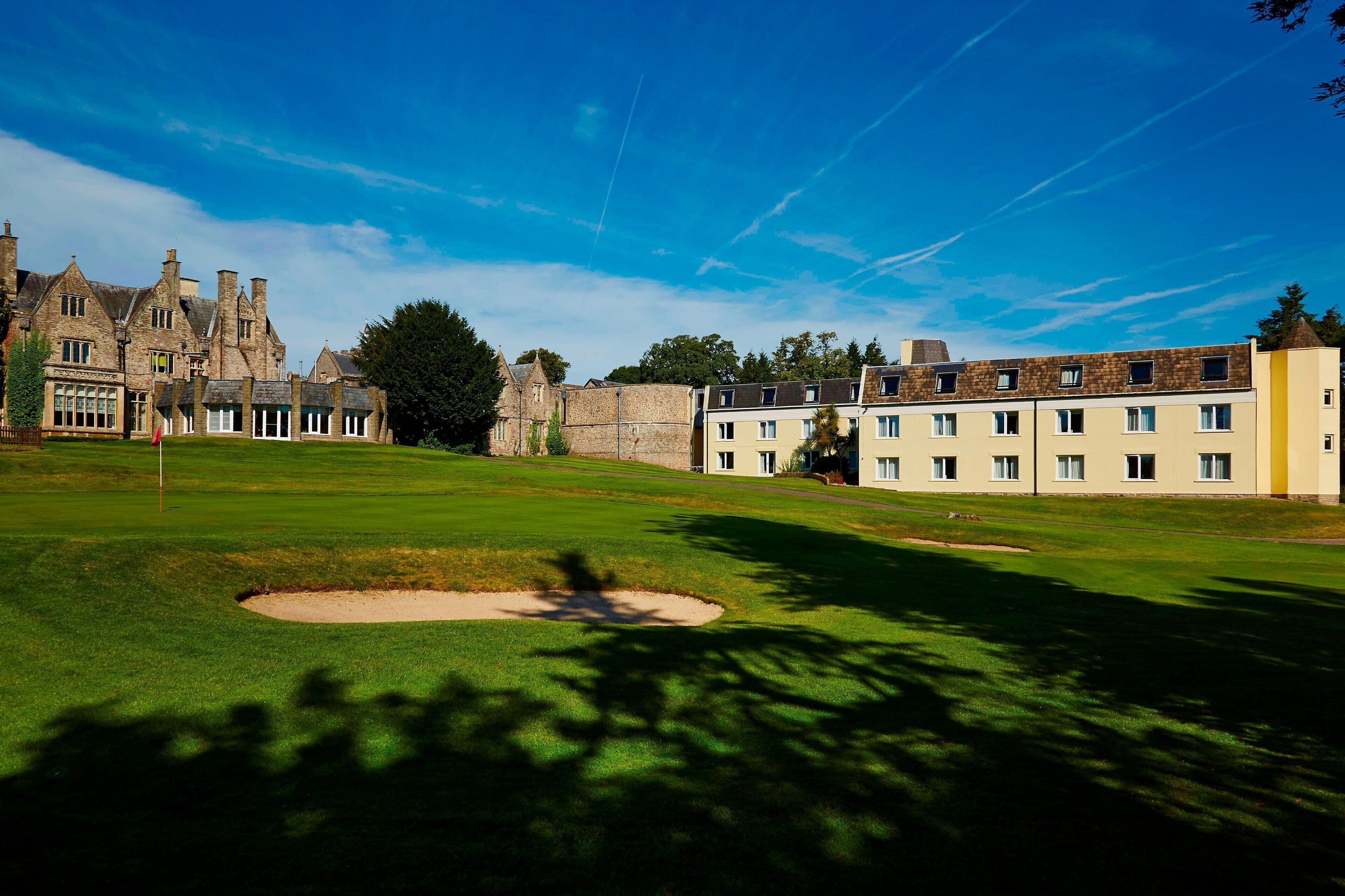 Un parcours de golf doté d’un club-house traditionnel, d’un bâtiment en pierre et d’un bâtiment moderne avec de nombreuses fenêtres.